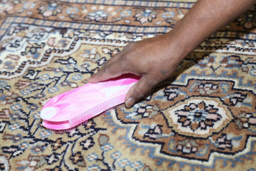 a person is cleaning a rug with a pink brush .